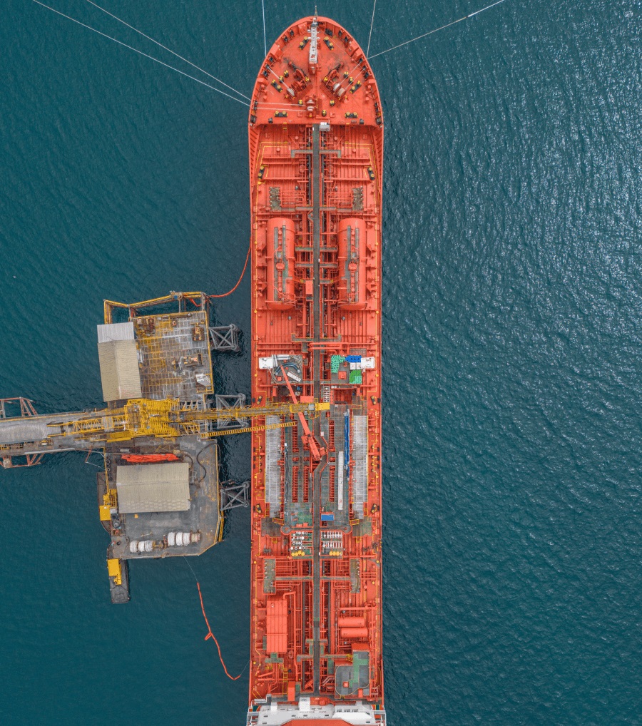 Aerial view of a large red cargo ship docked at an offshore platform in the ocean.
