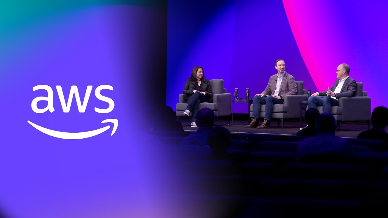Panel discussion on stage with AWS branding and a vibrant purple and pink background.