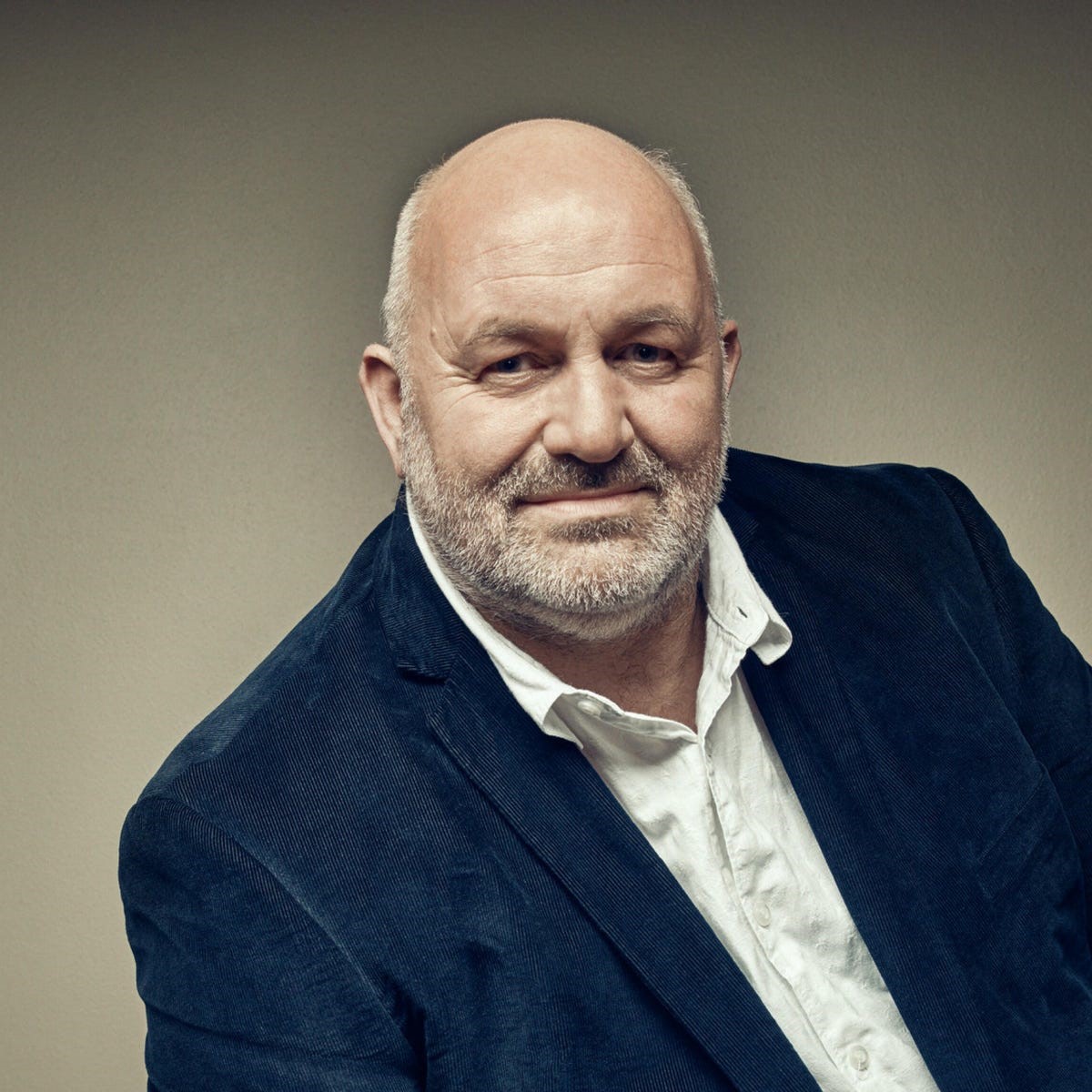 A person wearing a dark blazer over a white collared shirt against a neutral background.