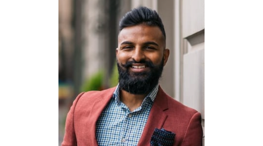 A person wearing a red blazer, checkered shirt, and pocket square, standing outdoors near a building.