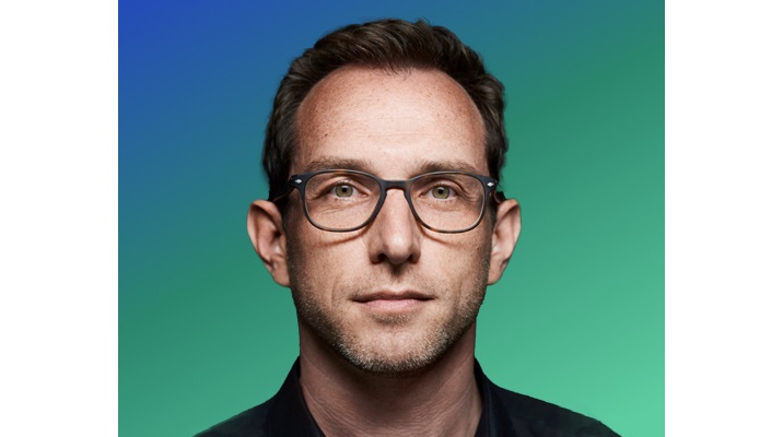 A person with short brown hair against a gradient blue-to-green background.