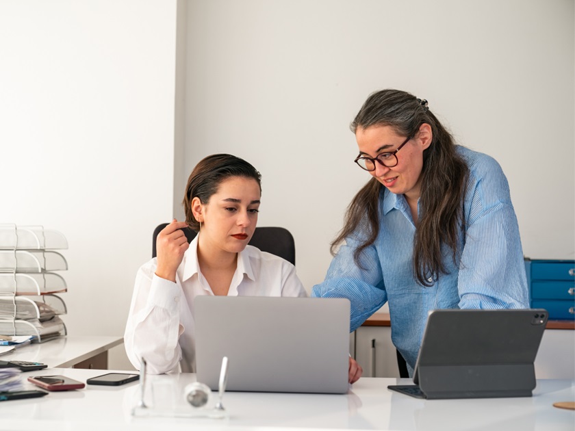 Two people working together at a desk with laptops and office supplies.