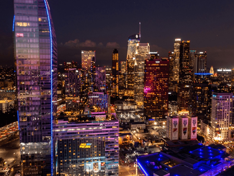 Nighttime cityscape of downtown Los Angeles with illuminated skyscrapers and vibrant lights.