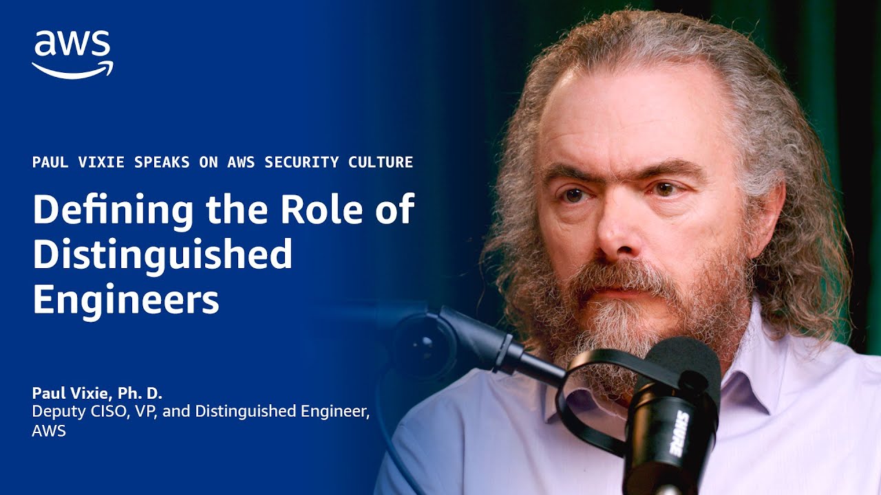 Text on a blue background reads "Defining the Role of Distinguished Engineers" with "Paul Vixie speaks on AWS security culture" above it; a microphone is visible in the foreground.