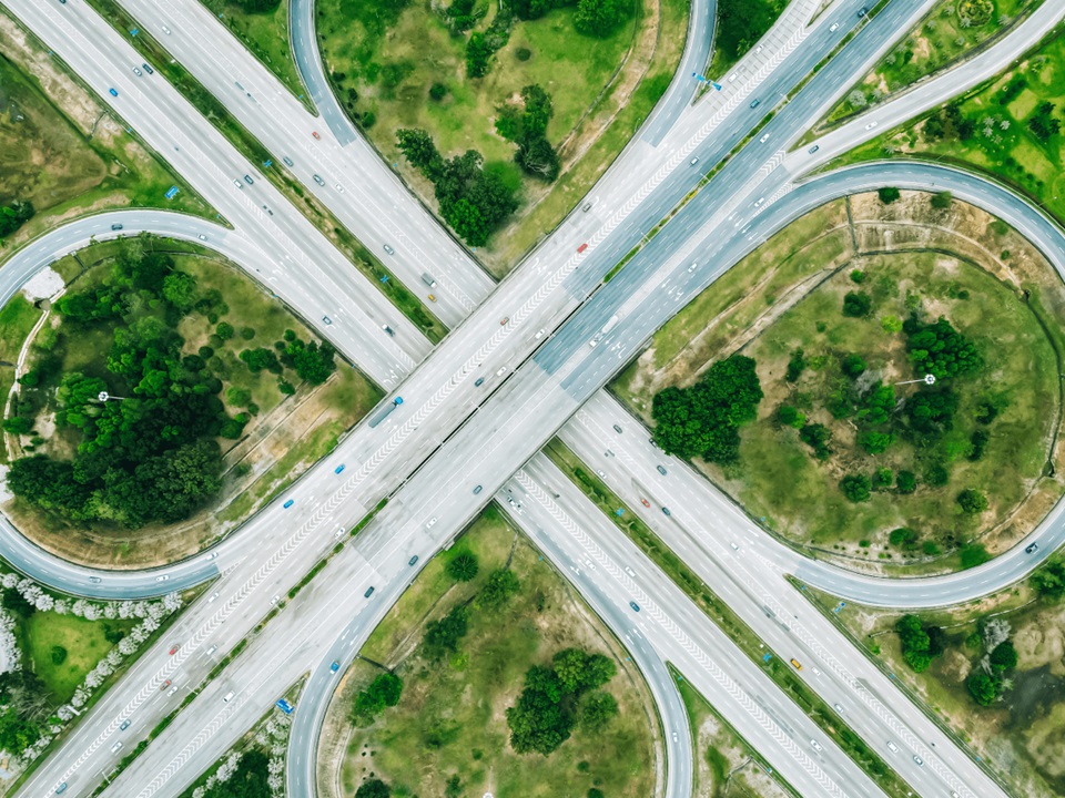 Aerial view of a highway interchange with looping ramps surrounded by green grass and scattered trees.