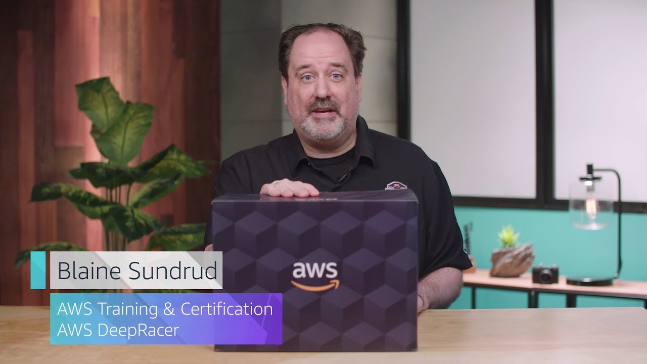 A YouTube video thumbnail featuring an instructor in an AWS Training & Certification DeepRacer session, holding an AWS-branded box, with the name 'Blaine Sundrud' and 'AWS Training & Certification, AWS DeepRacer' displayed on the screen.