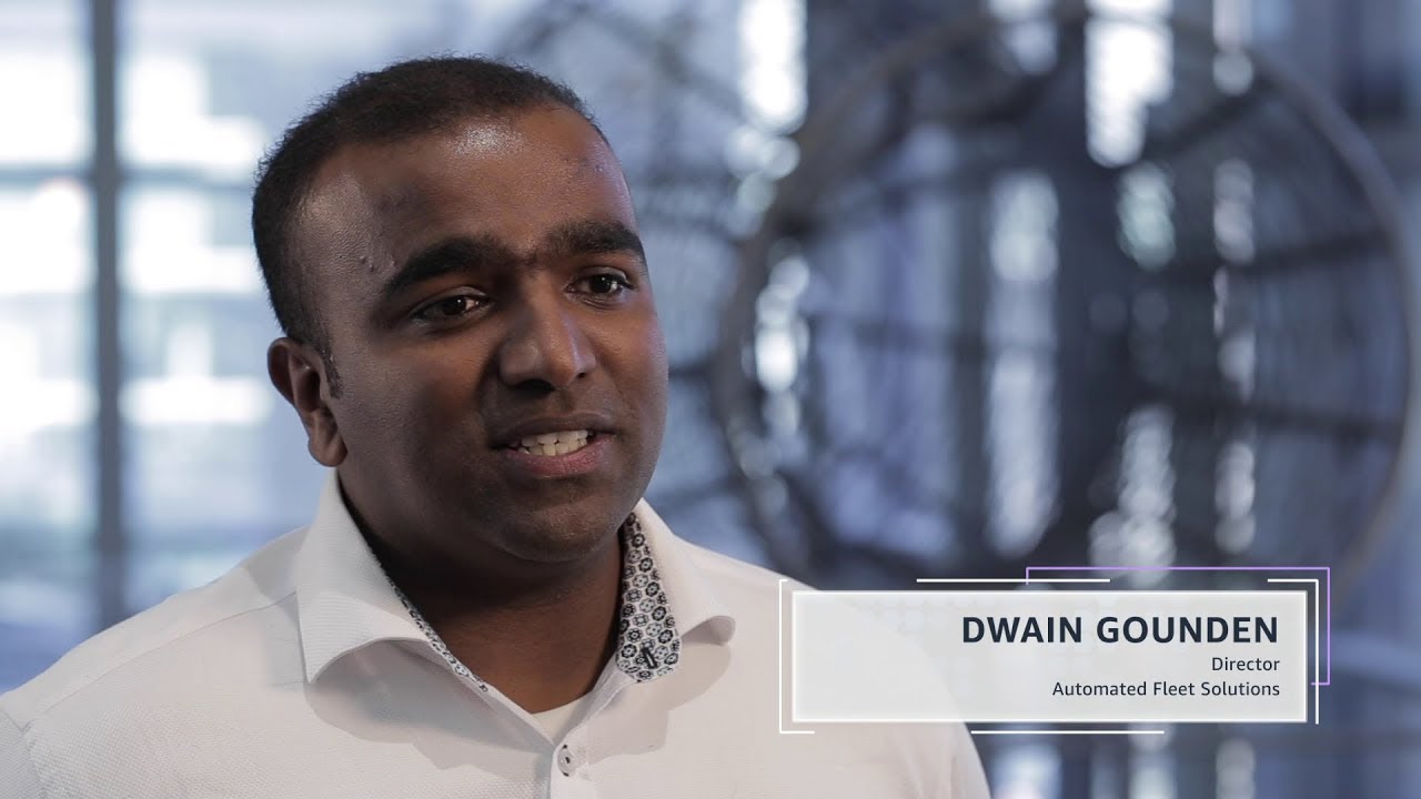 A YouTube video thumbnail showing a man in a white shirt, with overlay text stating 'Dwain Gounden, Director, Automated Fleet Solutions' on a blurred office background.