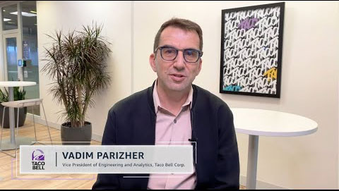 Vadim Parizher, Vice President of Engineering and Analytics at Taco Bell Corp., is sitting in an office setting with modern decor. A Taco Bell logo and his title are displayed on the screen.