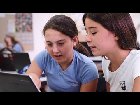 Two people sitting closely together, focused on a laptop in a classroom setting.
