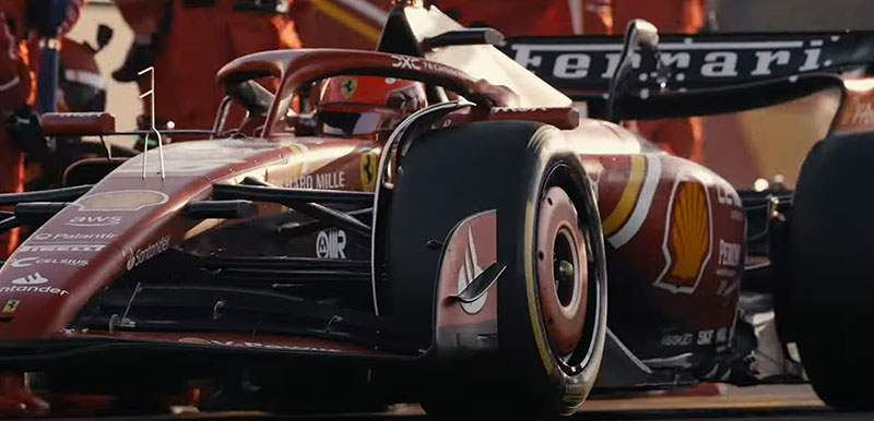 A close-up of a Ferrari Formula One car during a pit stop, with the Ferrari logo visible and pit crew members in the background.