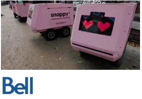 A row of pink, box-shaped delivery robots with heart-shaped eyes on their screens and 'snappy' branding, parked on a sidewalk with the Bell logo below.