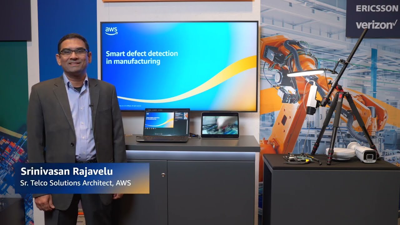 A demonstration setup for smart defect detection in manufacturing using AWS, shown with a presenter, robotics machinery, and monitoring equipment on display in an industrial environment.