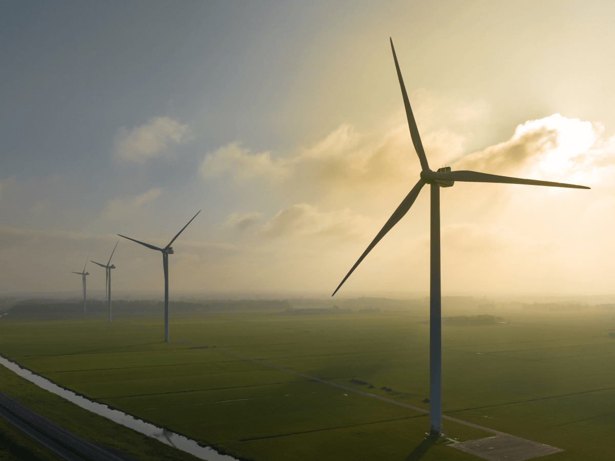 A row of large wind turbines generating power in a green field during sunset, illustrating clean energy and power utilities.