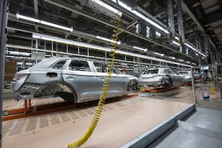 Automotive production line showing partially assembled car frames undergoing quality inspection in a manufacturing facility.