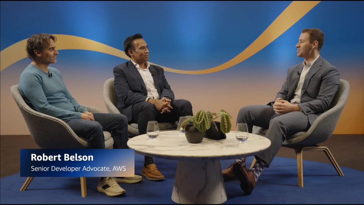 Thumbnail image for an AWS panel discussion featuring three individuals seated around a coffee table. The setting includes a modern studio with a blue and gold backdrop and a name caption identifying Robert Belson as Senior Developer Advocate, AWS.