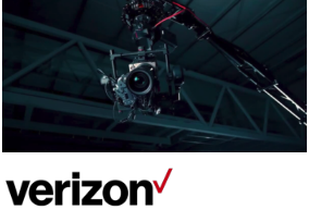 A professional camera rig suspended from a crane inside an industrial building, with the Verizon logo displayed below.