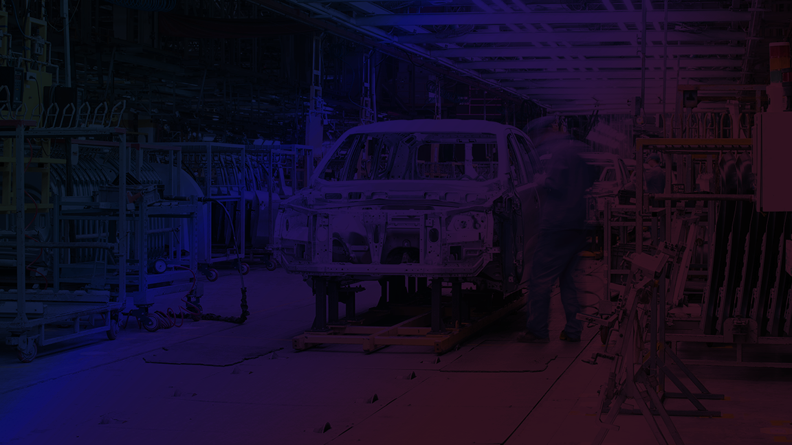 Automotive factory assembly line showing a car frame being assembled with workers and machinery in an industrial setting.