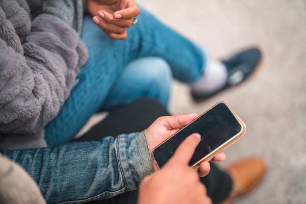 Closeup view of a person using a smartphone while sitting outdoors in casual clothing.