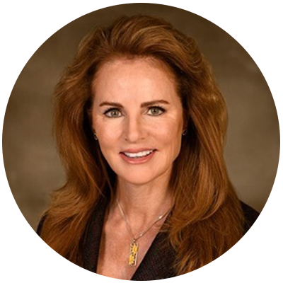 Professional headshot portrait of a woman with long reddish-brown hair, wearing a dark business jacket, photographed in front of a plain brown background.