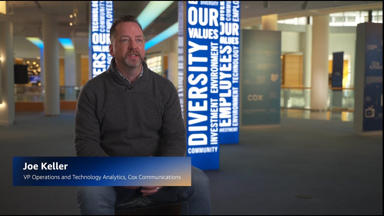 YouTube thumbnail image featuring Joe Keller, VP Operations and Technology Analytics at Cox Communications, seated for an interview with branded pillars in the background.