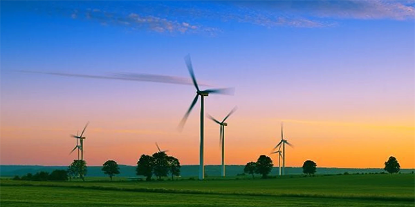 Wind turbines in a green field at sunset with a colorful sky.