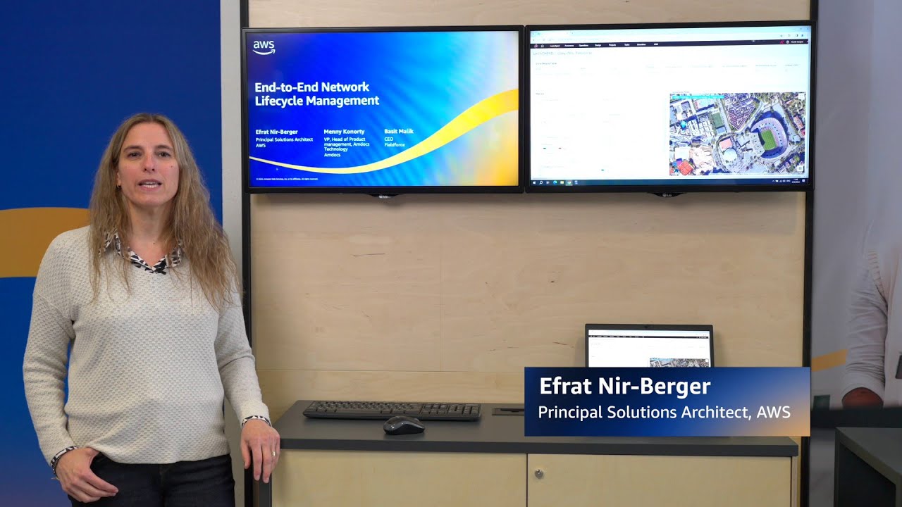 YouTube thumbnail featuring a person standing next to two monitors displaying 'End-to-End Network Lifecycle Management' as part of an AWS presentation, with the name 'Efrat Nir-Berger, Principal Solutions Architect, AWS' shown on screen.
