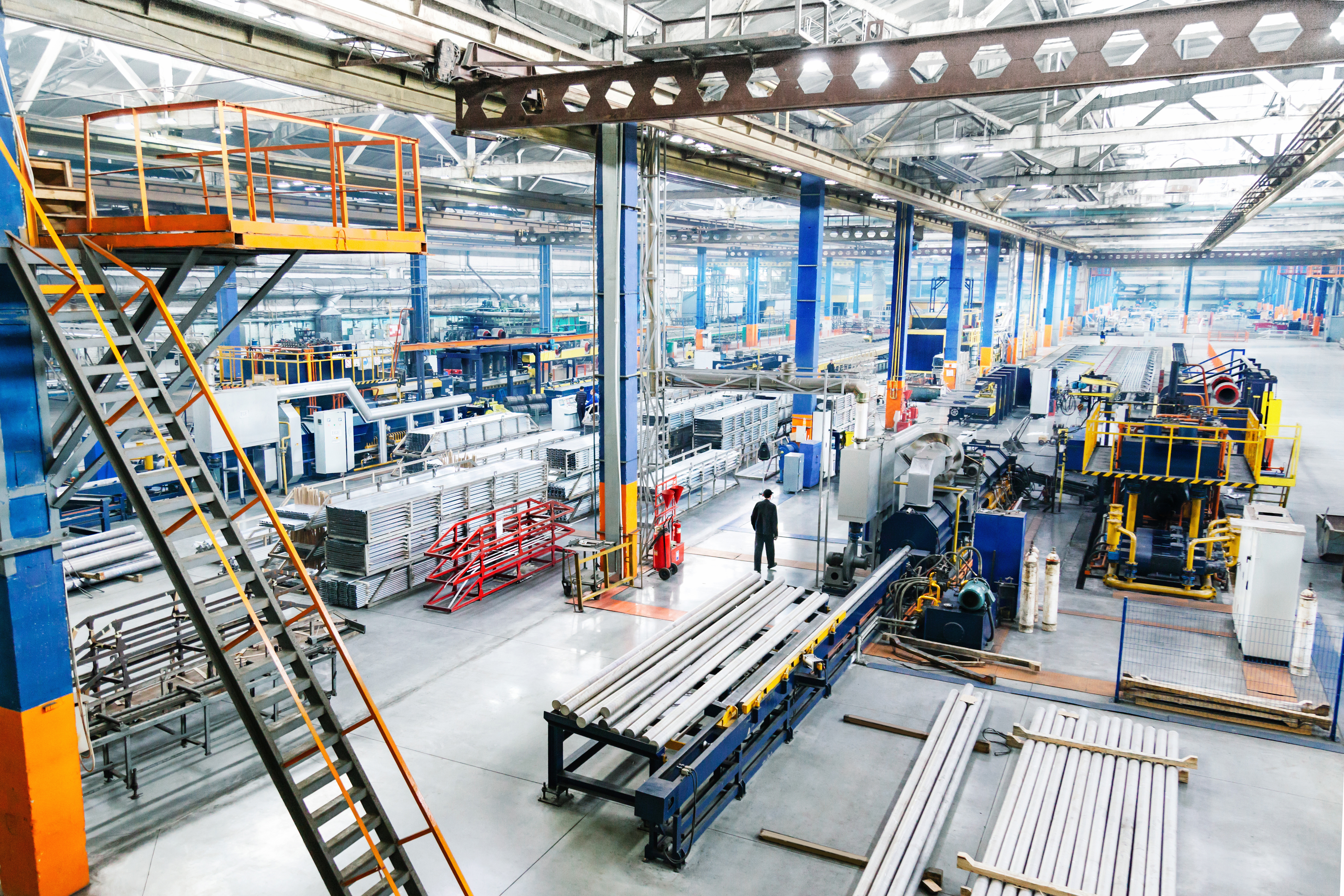 Large industrial factory interior with machinery, metal materials, and a worker walking through the space.