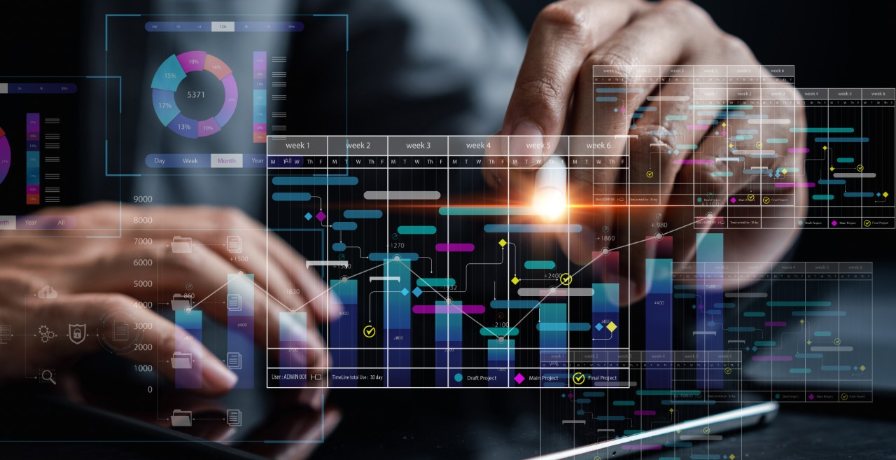 Hands using a tablet with overlaid digital dashboards and data visualizations illustrating industrial end-to-end data strategy concepts, including charts, graphs, and project timelines.