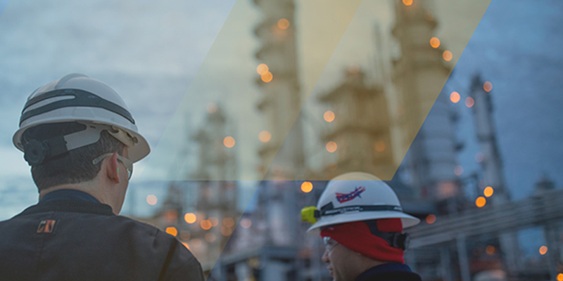Two industrial workers wearing safety helmets are seen at an industrial plant or refinery, with blurred lights and smokestacks in the background. The image conveys a modern industrial environment, possibly illustrating customer or employee activities at Invista.