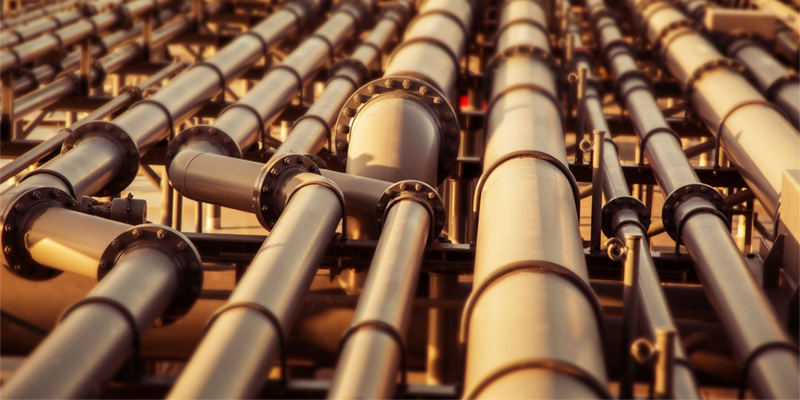 A network of industrial metal pipelines illuminated by warm sunlight.