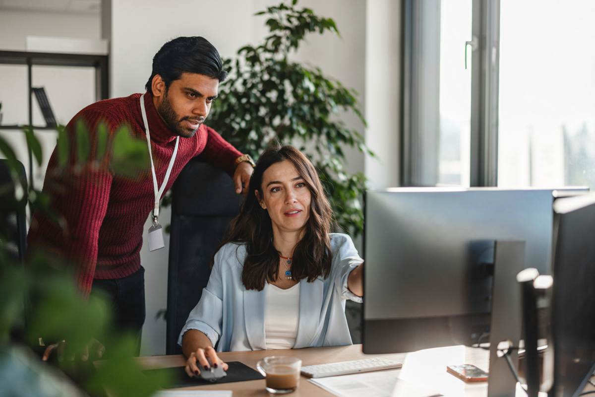 Two office coworkers collaborating and discussing revenue fraud prevention while working at a computer in a modern office environment.