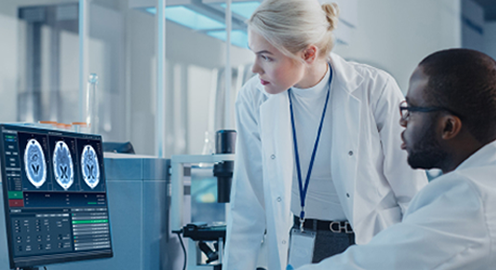Two medical professionals in a lab reviewing brain scan images on a computer screen.