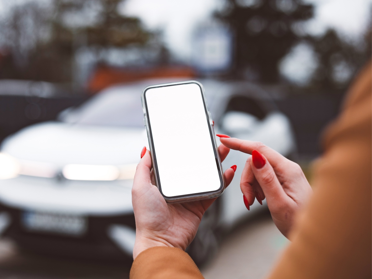 A person holds a smartphone with a blank screen while standing beside a parked car