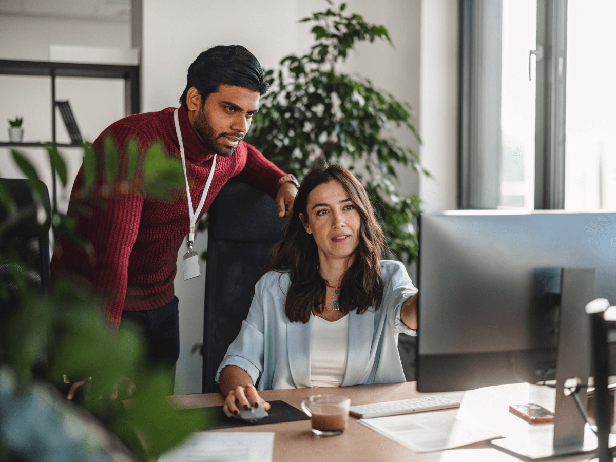 Two colleagues review information together on a desktop monitor in an office