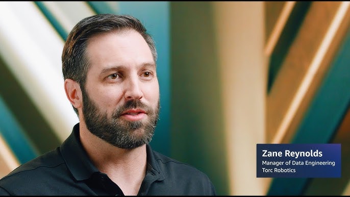 Zane Reynolds, Manager of Data Engineering at Torc Robotics, speaking in front of a blurred, color-striped background.