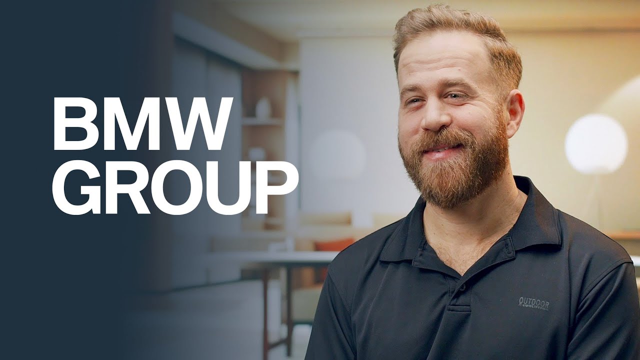 A man with a beard smiles in a professional interview setting with the text 'BMW GROUP' displayed on the left side of the image.