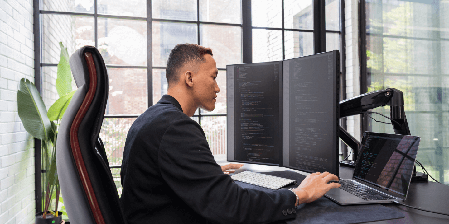Man of color working on laptop and two monitors