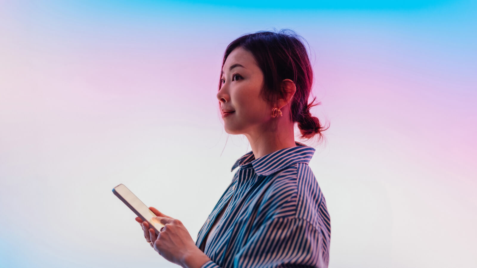 A woman holding and using a smartphone, standing in front of a blue and pink gradient background.