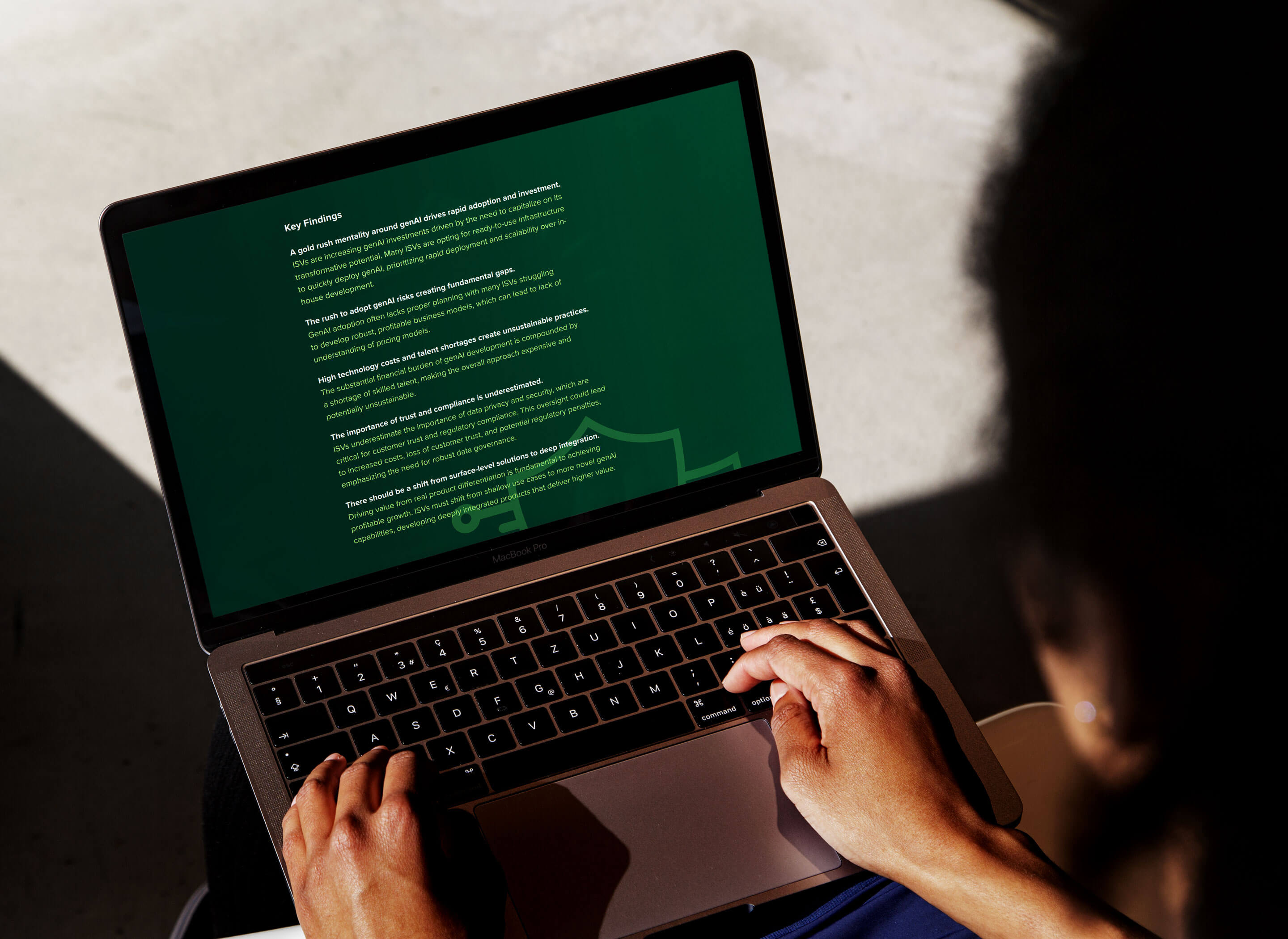 Hands typing on a laptop displaying text on a green screen, with sunlight casting shadows on the surface.