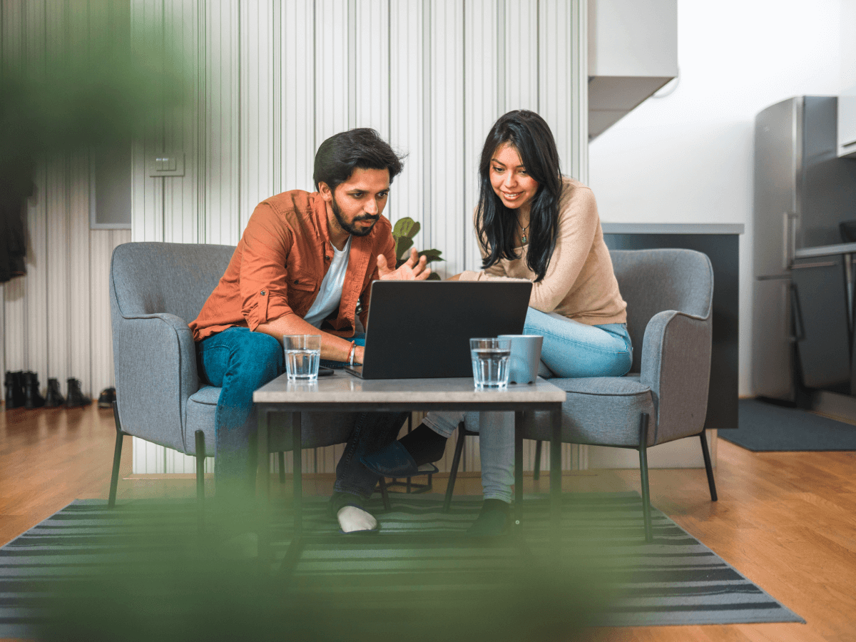 Two people sitting on a sofa using a laptop together in a modern living room setting.