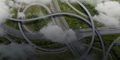Aerial view of a complex highway interchange surrounded by greenery and partially covered by clouds.