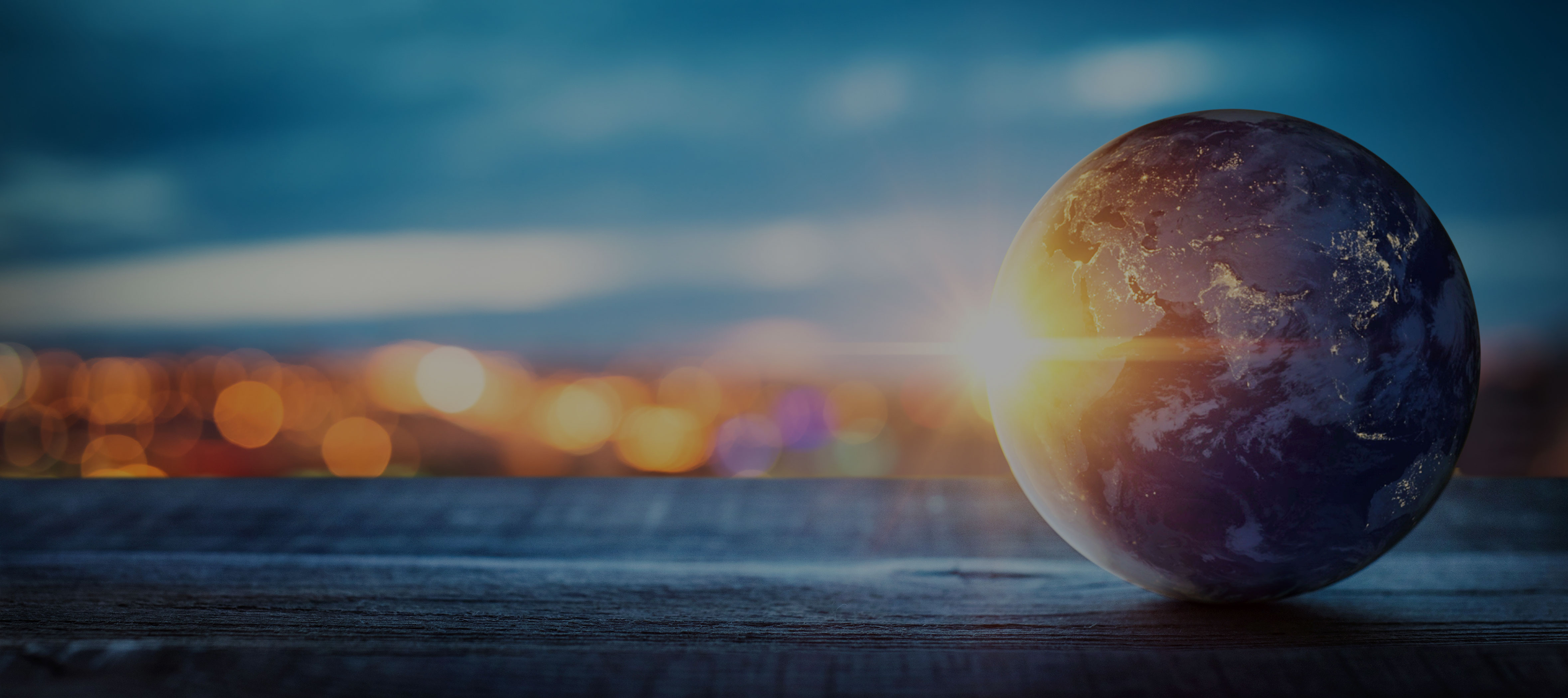 A globe of the Earth sits on a table with a sunrise in the background, set against a blurred cityscape and blue sky.