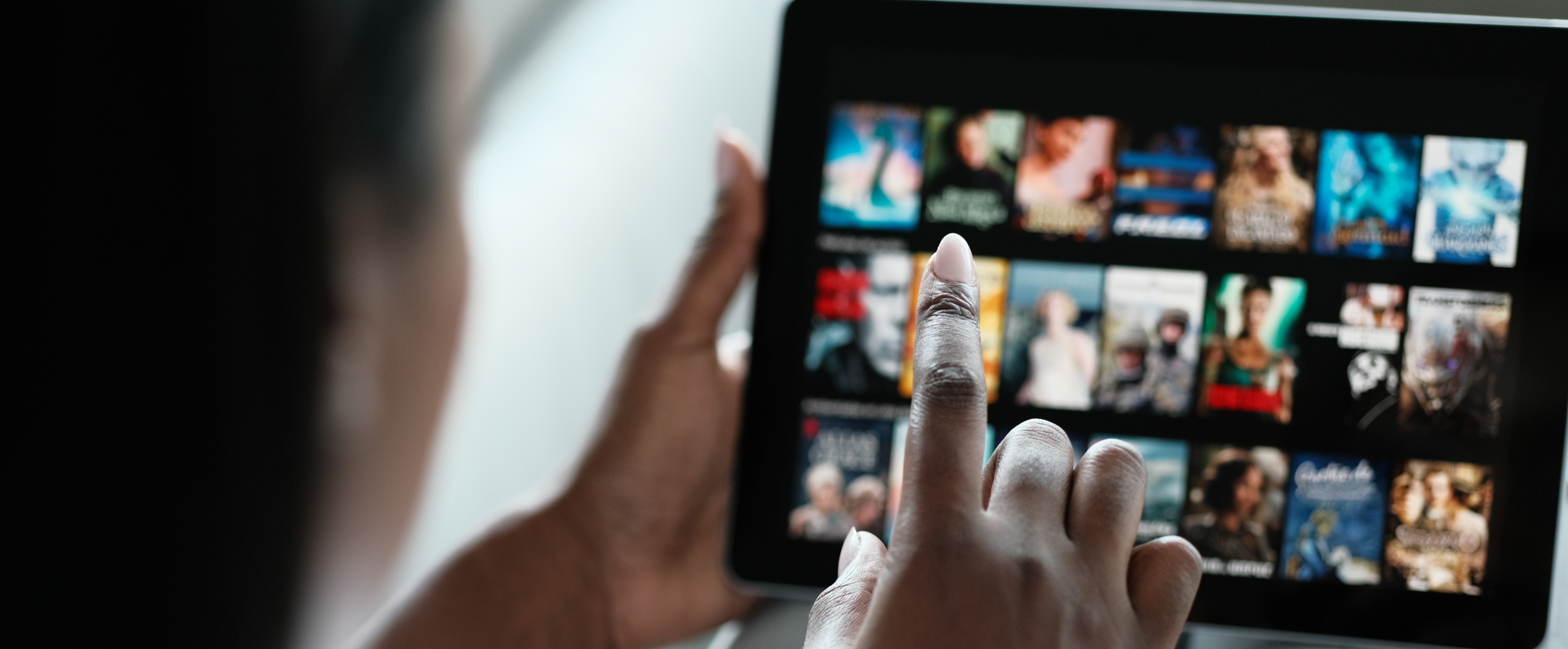A woman using a tablet to browse through a selection of movies on a streaming service.