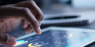 A close-up of a hand interacting with a digital financial dashboard on a tablet, illustrating the use of AWS Cloud for financial data and analytics.