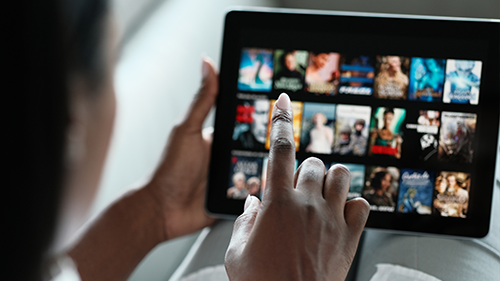 A person is interacting with a tablet displaying a streaming media app showing entertainment content.