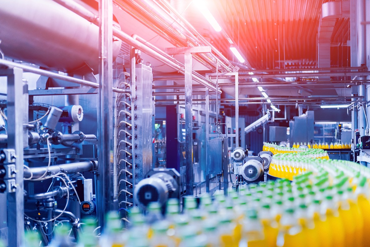 An automated beverage bottling production line inside a modern factory, showing a conveyor belt with bottles and industrial machinery.