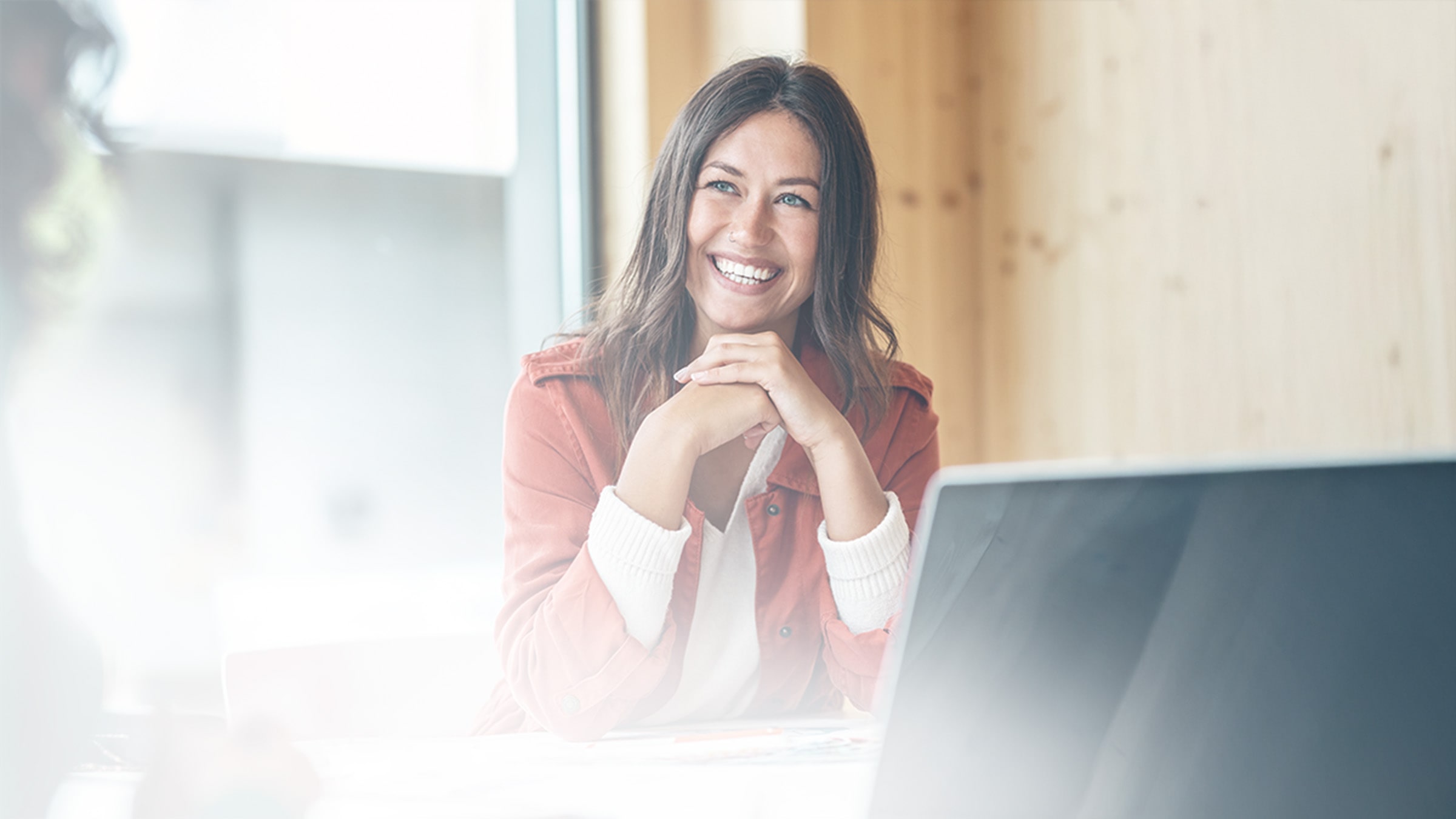 General_public_services_hero_white_scrimmage_smiling-woman-in-orange-jacket-at-desk.