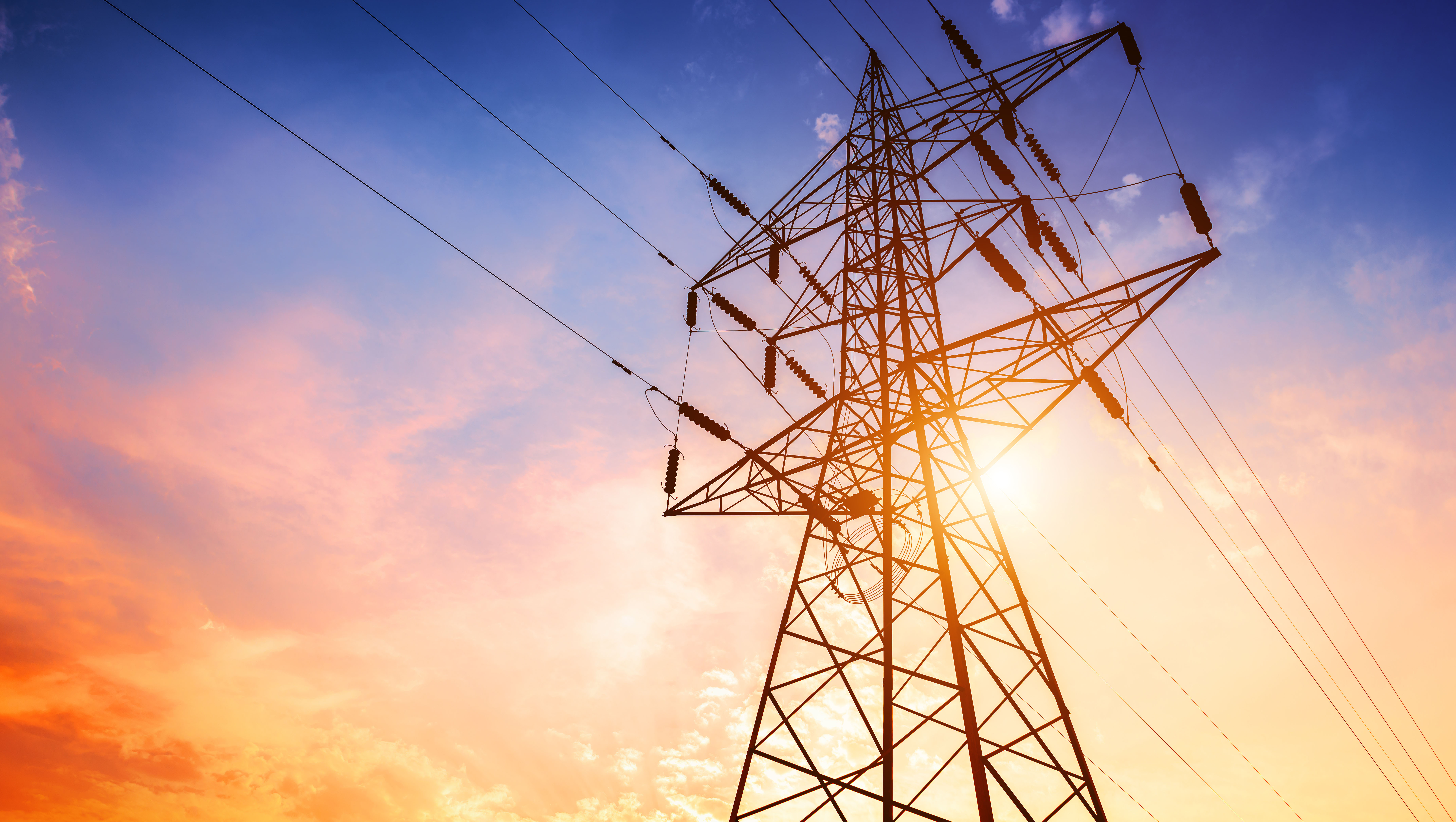 A high voltage powerline tower silhouetted against a vibrant sunset sky, illustrating energy infrastructure and electricity transmission.
