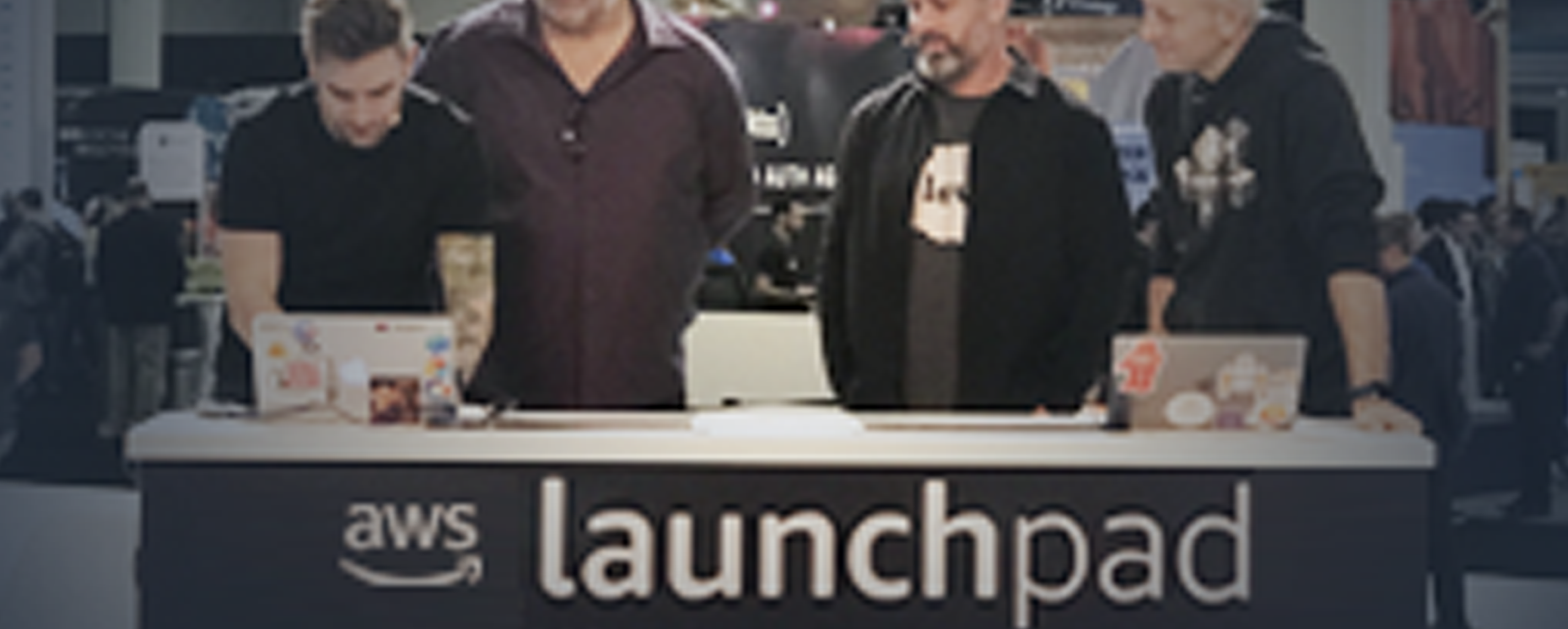 Four people participate in a panel discussion at the AWS Launchpad event, standing behind a desk with laptops in front of an audience.