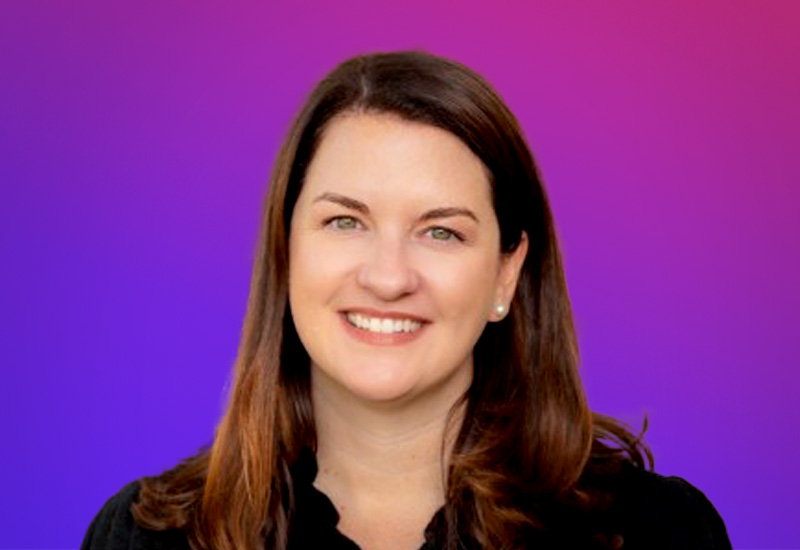 A person with long brown hair wearing a black top, set against a gradient purple and pink background.